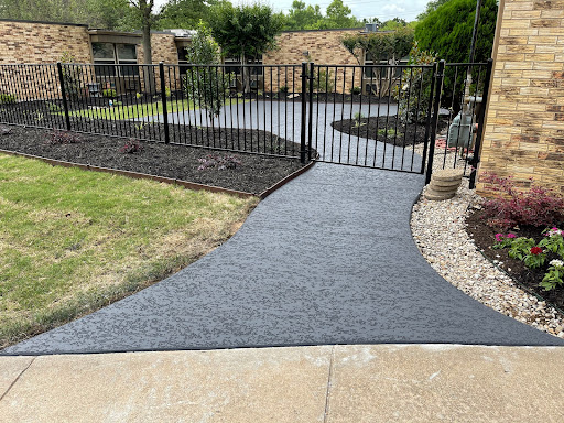 A newly paved concrete pathway leading to a fenced area in a landscaped garden.