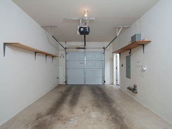 An empty garage with a closed overhead door and wall-mounted shelves.