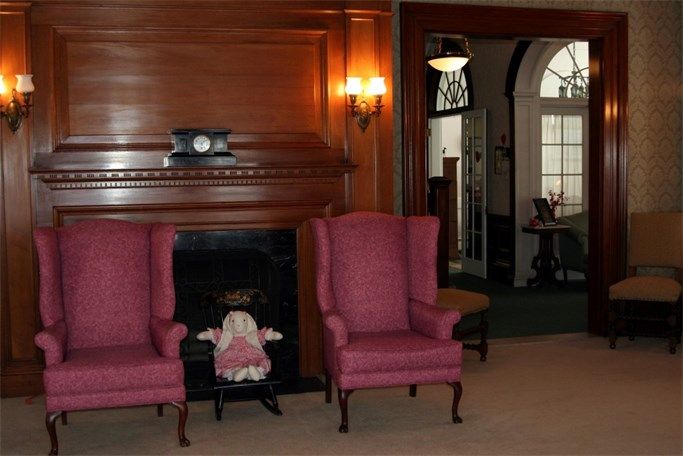 A traditionally decorated room with a fireplace, two armchairs, and a doll placed between them.