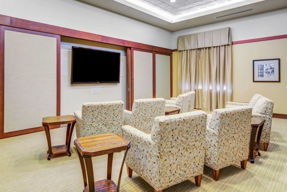 A cozy living room with patterned chairs arranged around a television, complemented by wooden side tables and elegant curtains.