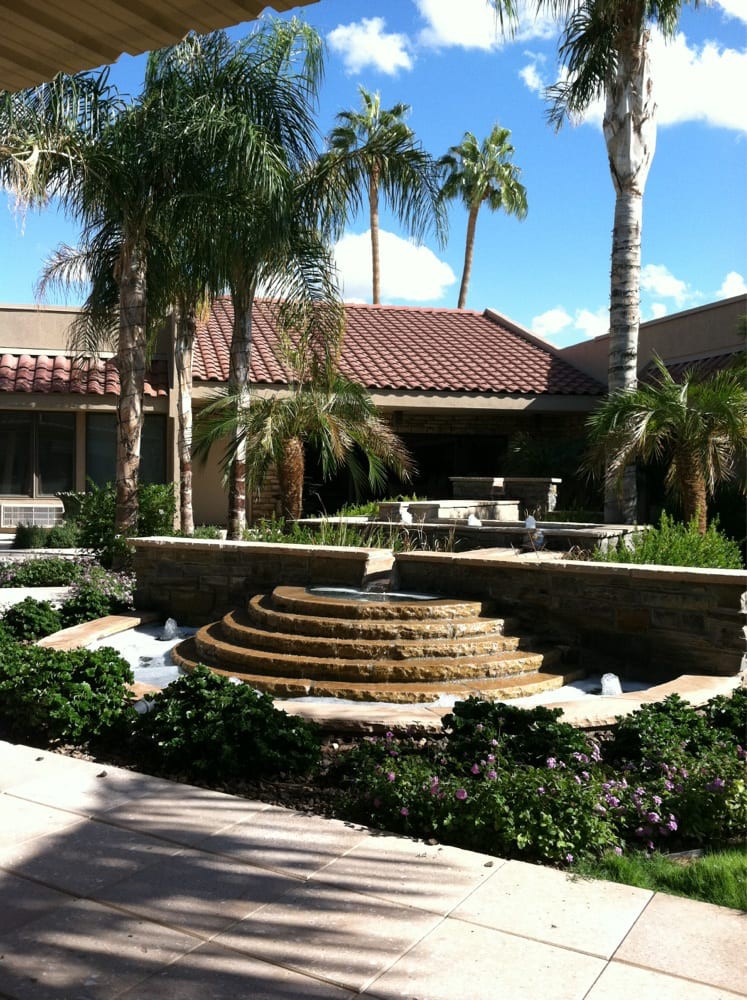 A serene courtyard featuring a tiered fountain surrounded by lush palm trees and well-maintained landscaping.