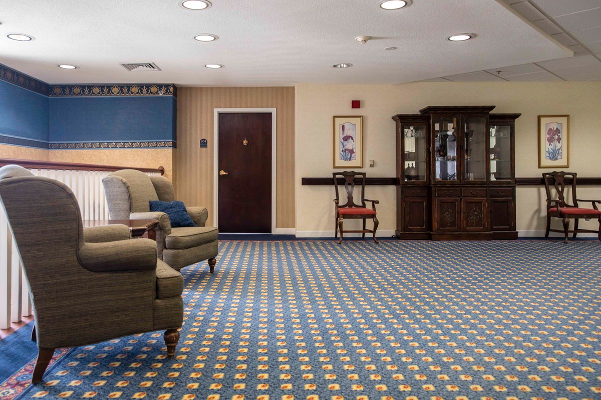 A cozy living room with patterned carpet, armchairs, and a cabinet.