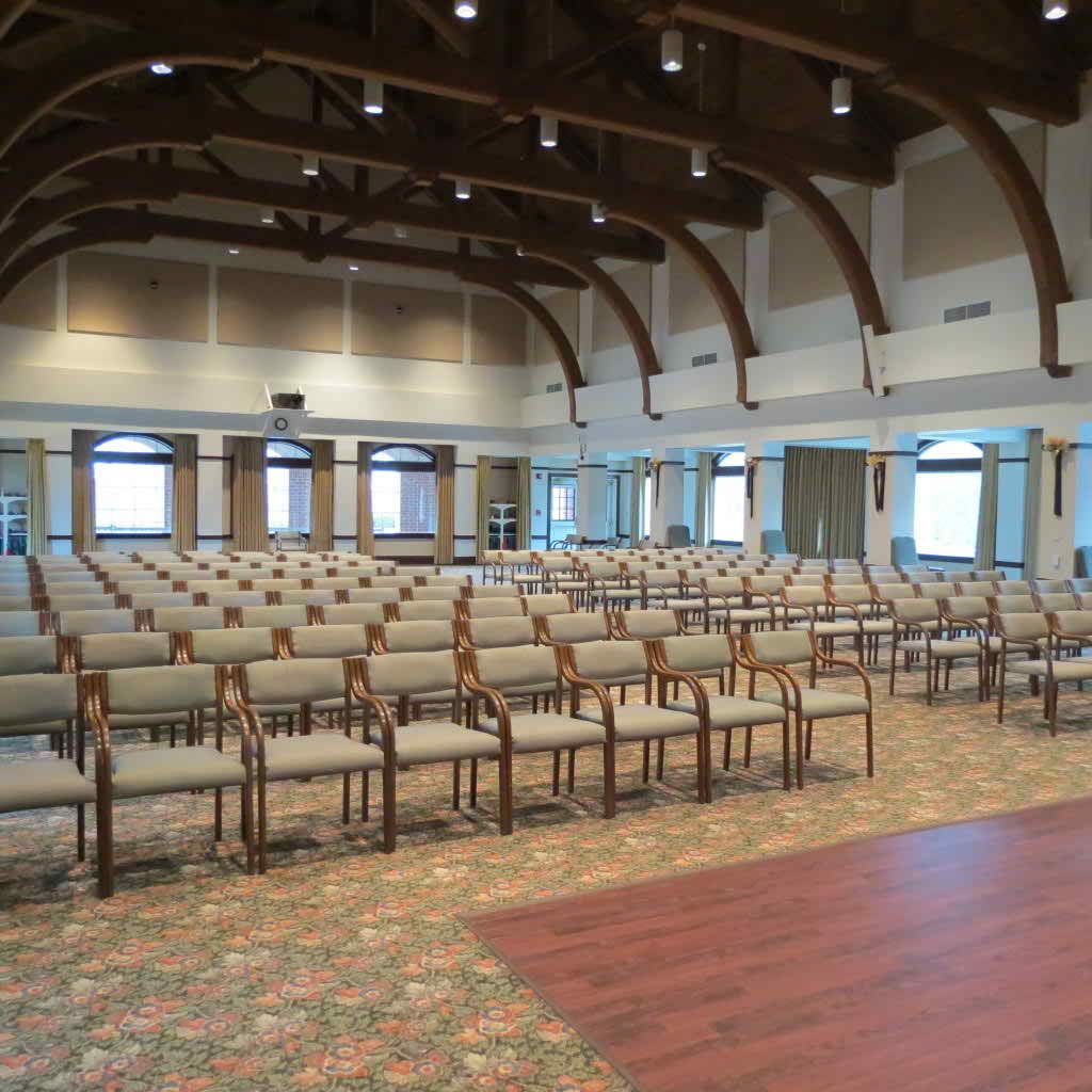 An empty auditorium with rows of chairs and a wooden stage.