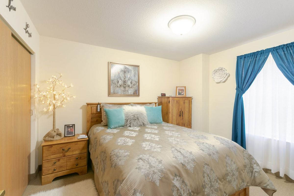 A cozy bedroom with a wooden bed and matching furniture, decorated with a painting and a unique lamp.