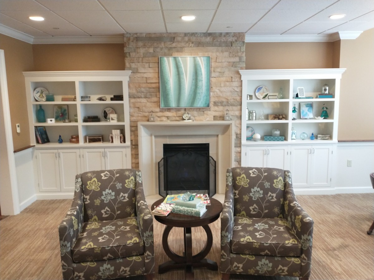 A cozy living room with a stone fireplace, two patterned chairs, and built-in bookshelves.