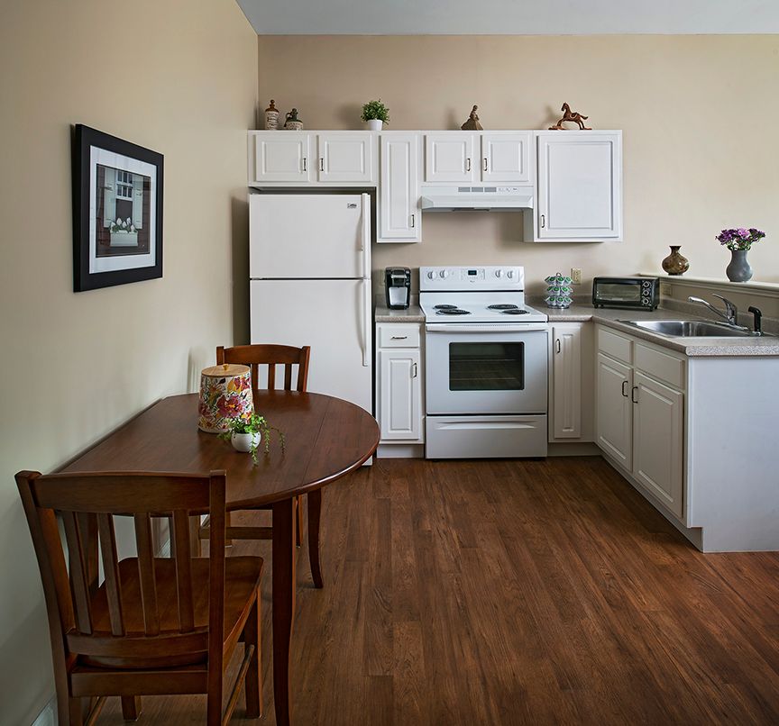 A cozy kitchen with white cabinets, featuring a small dining table and chairs on a wooden floor.