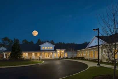 A well-lit building with a circular driveway under a clear night sky and a full moon.