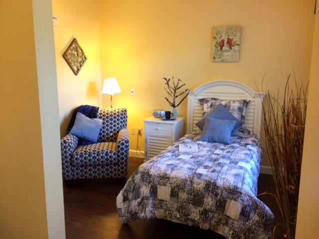 A cozy bedroom with a single bed and an armchair, warmly lit by a lamp.