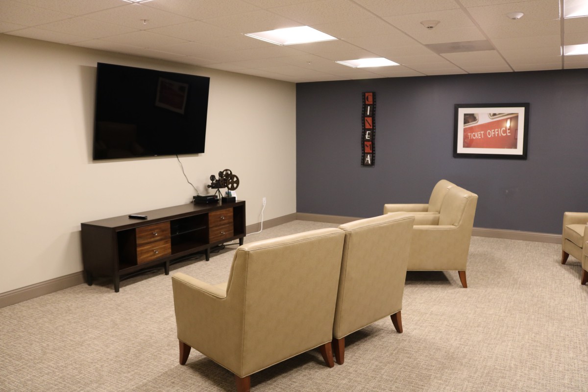 A modern living room with beige armchairs, a wall-mounted TV, and minimalist decor.