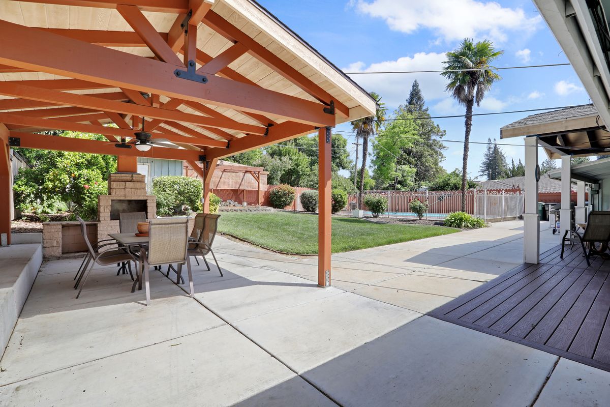 A spacious backyard with a covered patio area and outdoor dining set, surrounded by a well-maintained lawn and palm trees.