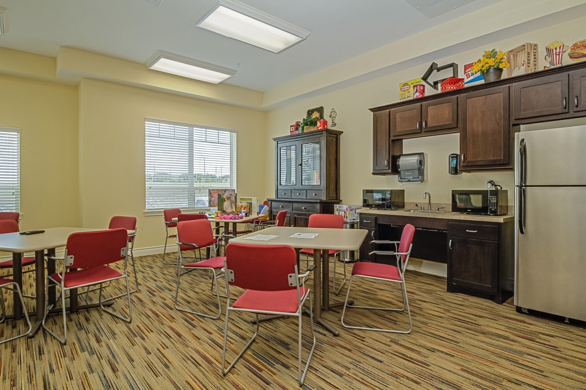 A bright and modern break room featuring red chairs, tables, and kitchen appliances.