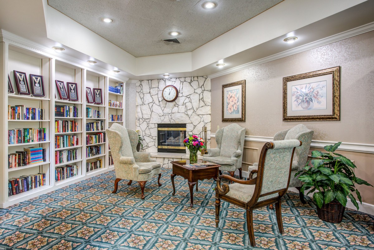 A cozy library seating area with a fireplace surrounded by bookshelves and comfortable chairs.