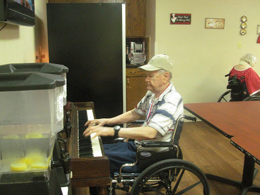 An elderly man enjoying a moment of music at the piano in a wheelchair.