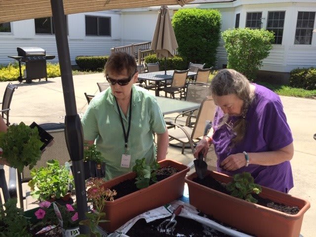 Two people enjoying a sunny day while planting flowers in outdoor planters.