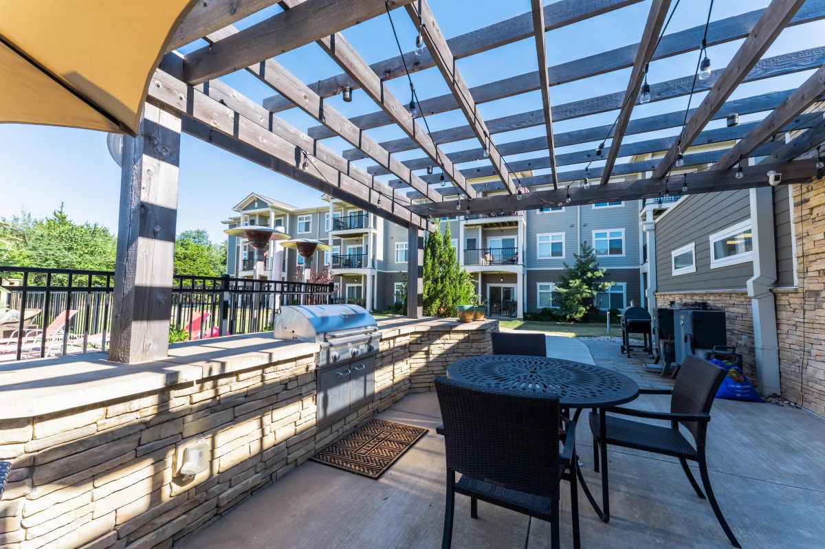 A sunny outdoor patio with a pergola and seating area in a residential apartment complex.