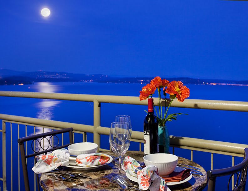 A romantic dinner setup on a balcony overlooking the ocean under moonlight.