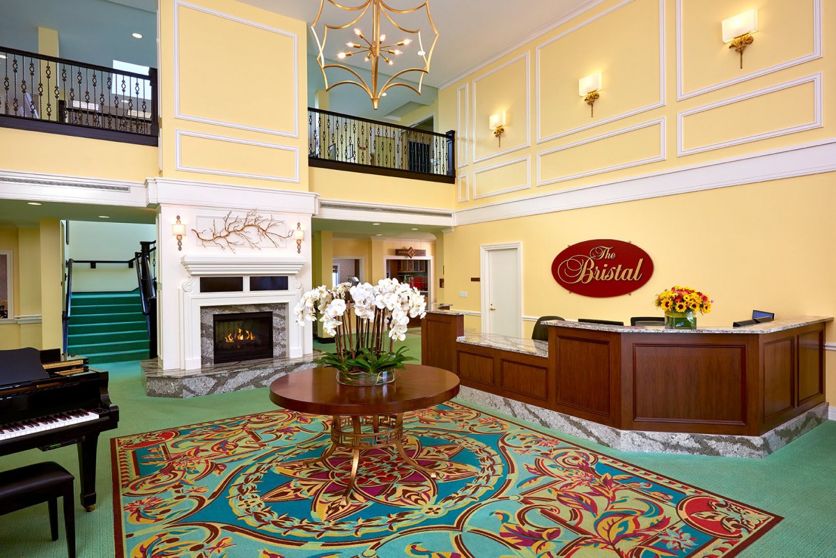A luxurious hotel lobby featuring a chandelier, fireplace, and reception desk with vibrant carpeting.