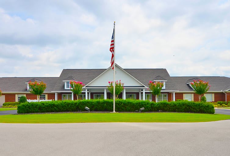 A large building with a flagpole flying the American flag in front, surrounded by greenery under a cloudy sky.