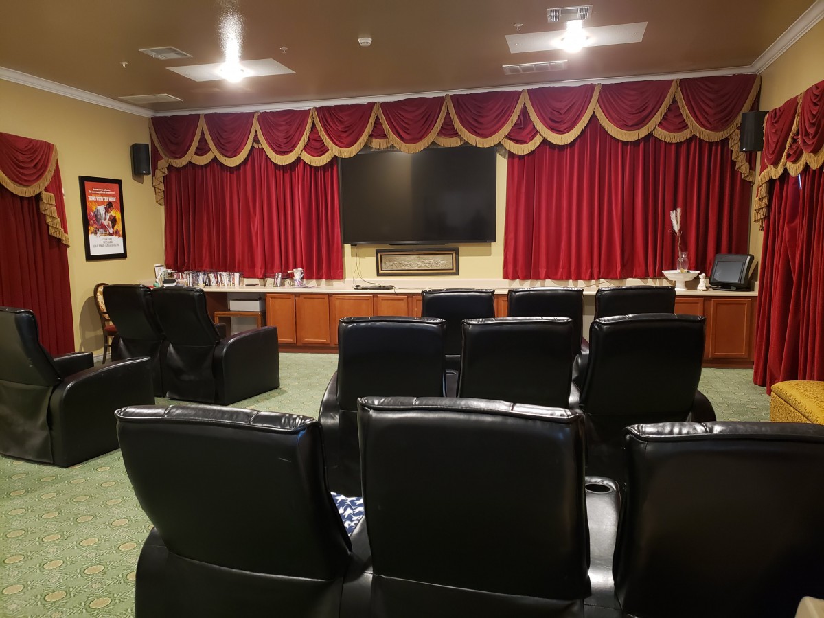 A cozy home theater setup with black leather seating and a large screen, framed by elegant red curtains.