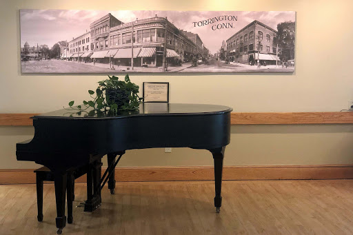 A black grand piano positioned near a historical mural, complemented by indoor plants.