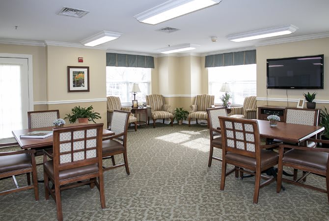 A well-lit seating area with tables and chairs, featuring large windows and indoor plants.