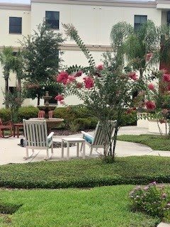 A tranquil garden setting with white chairs, vibrant flowers, and a fountain in the background.