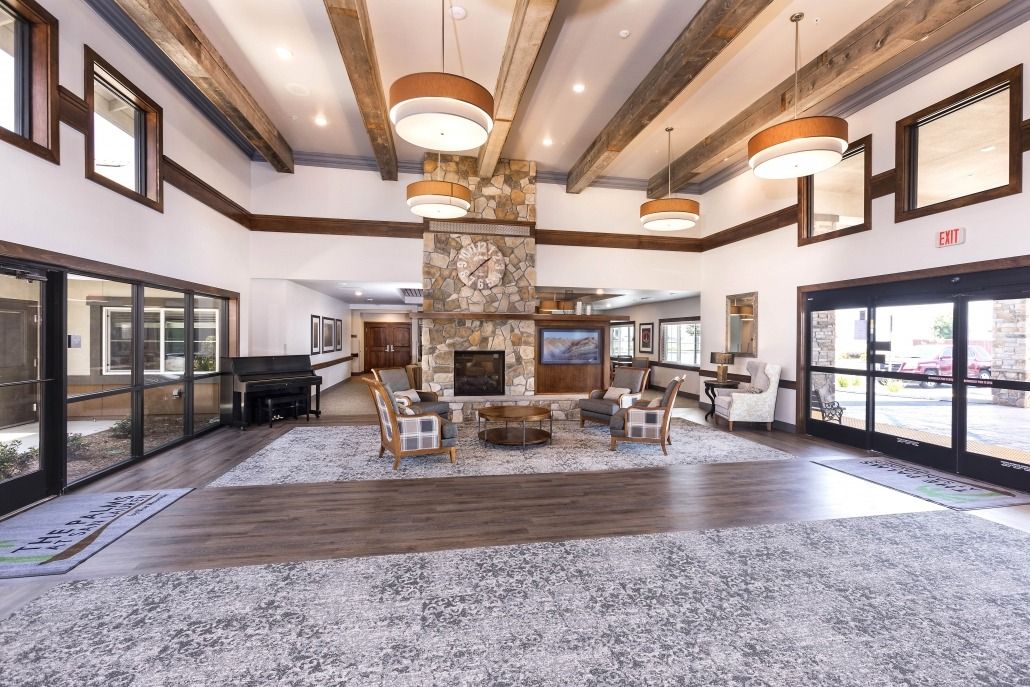 A spacious living room with a central stone fireplace, modern furniture, and wooden ceiling beams.