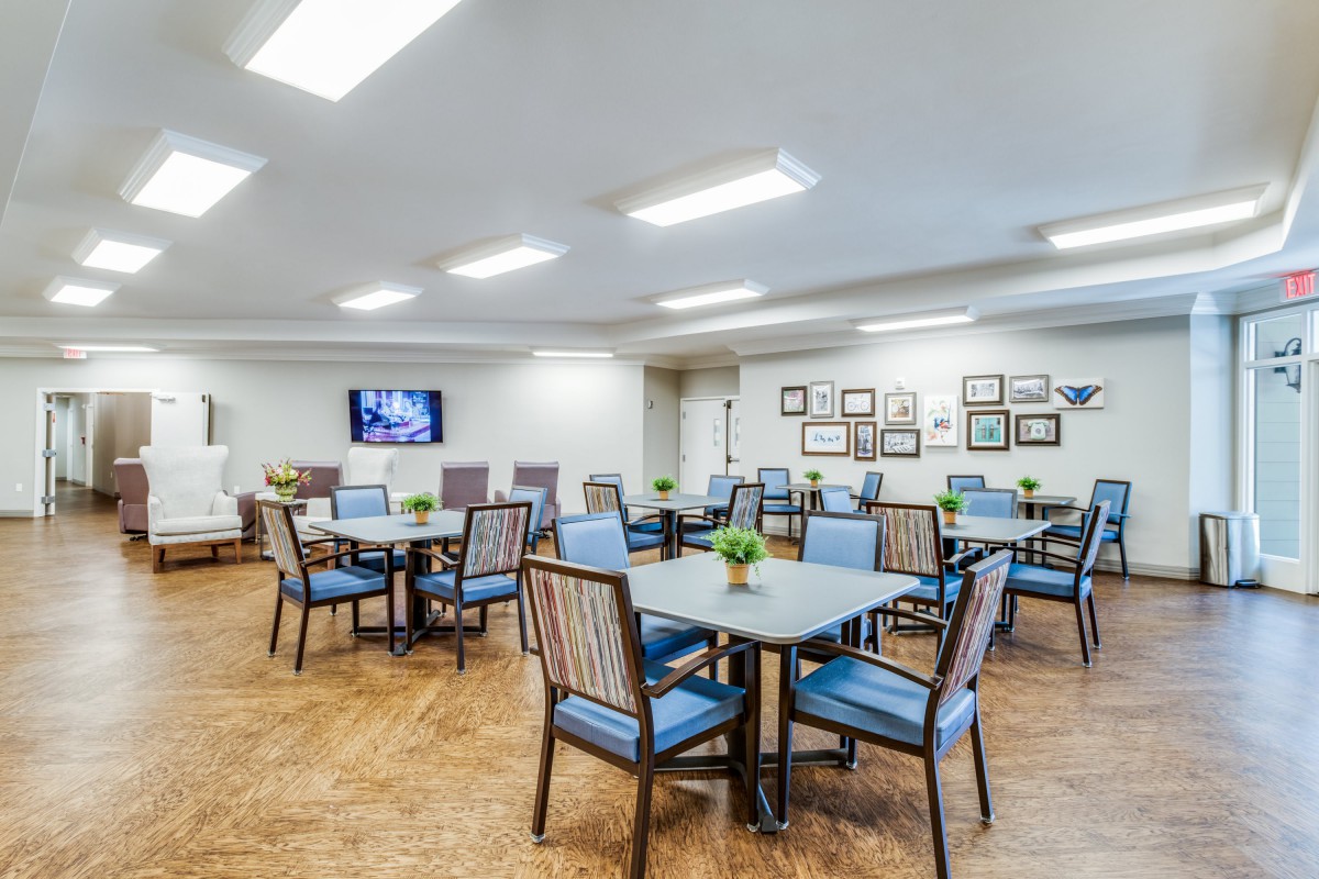 A bright and spacious dining area with neatly arranged tables and chairs, adorned with simple decor and lit by overhead lighting.