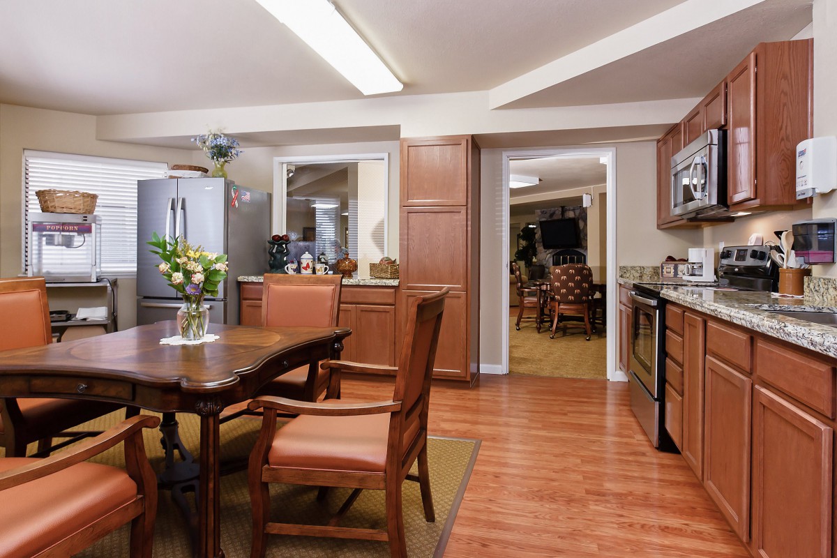 A modern kitchen with wood flooring, featuring a dining table with chairs and stainless steel appliances.
