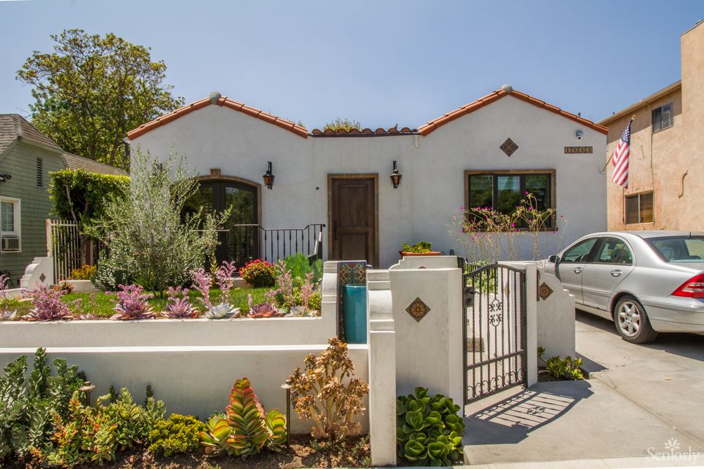 A charming house with a well-maintained garden and gated entrance on a sunny day.