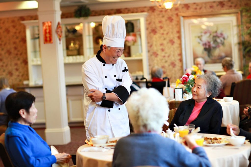 A chef interacting with senior patrons in a cozy restaurant setting.