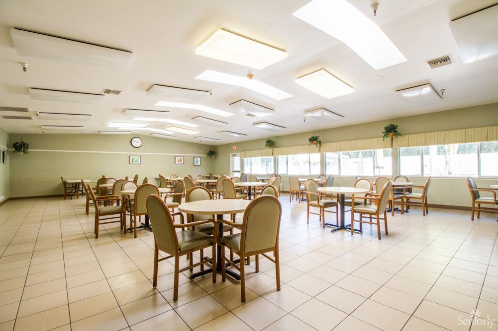 An empty dining area with multiple tables and chairs, illuminated by overhead light fixtures.