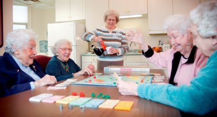 A group of seniors enjoying a game of Monopoly while having tea.