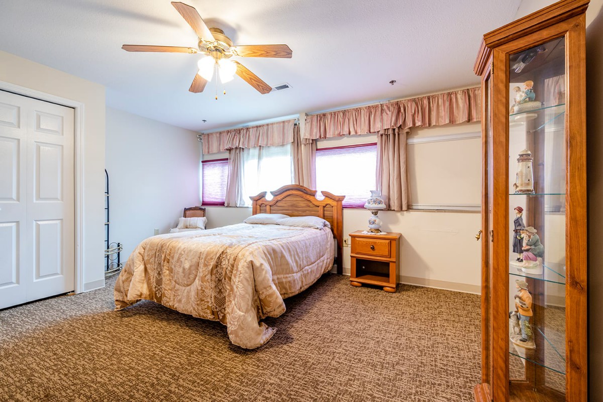 A cozy bedroom with a comfortable bed, nightstand, ceiling fan, and carpeted floor.