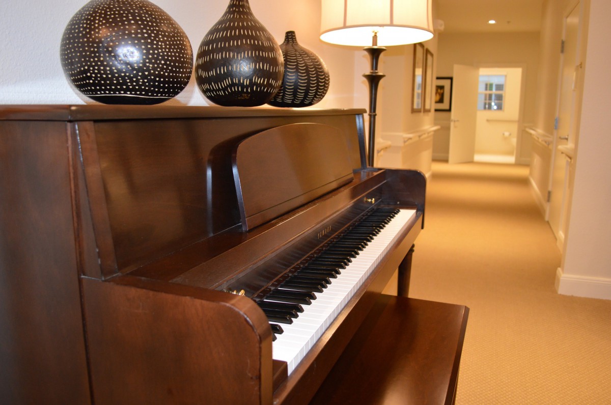 A well-decorated room featuring a polished upright piano with decorative vases and a lamp.