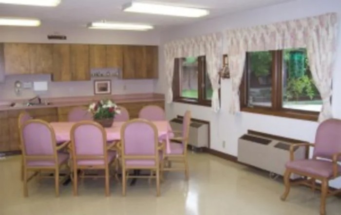 A cozy dining room with a table and pink chairs, adorned with a flower vase.