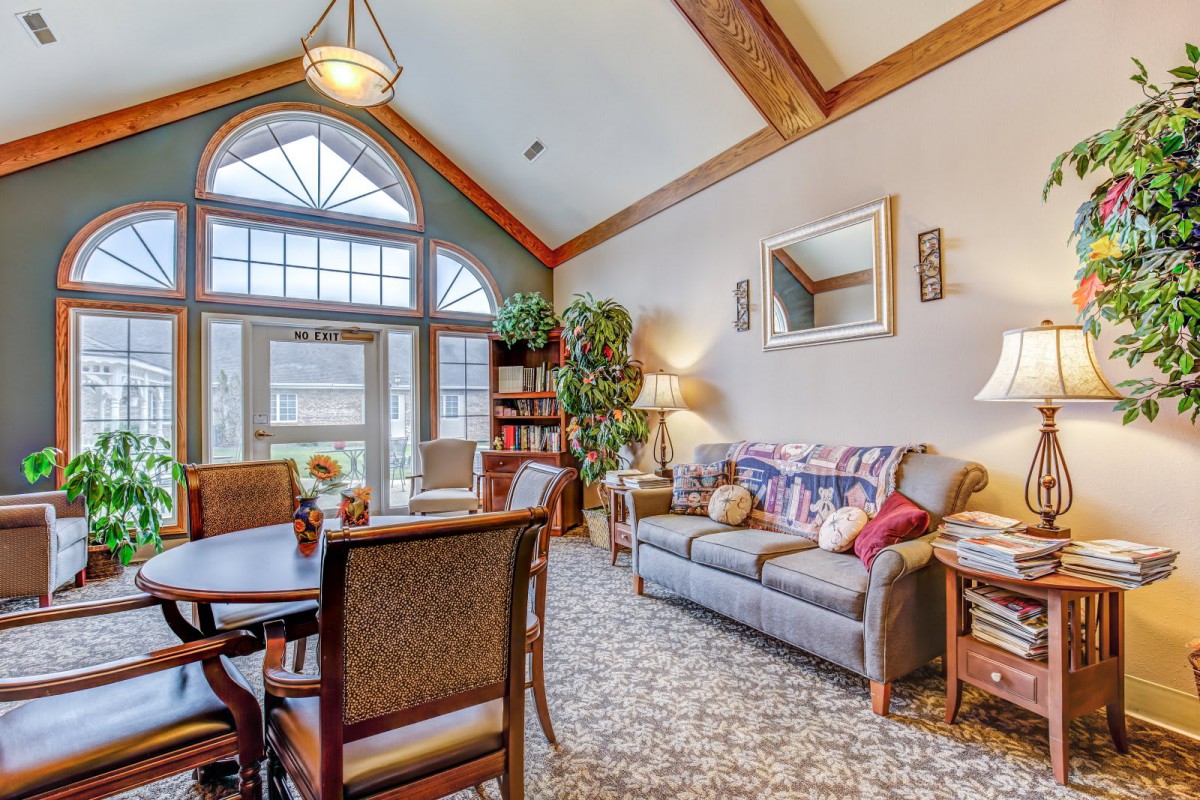 A cozy living room featuring a sofa, dining table with chairs, and decorative elements like plants and a mirror.