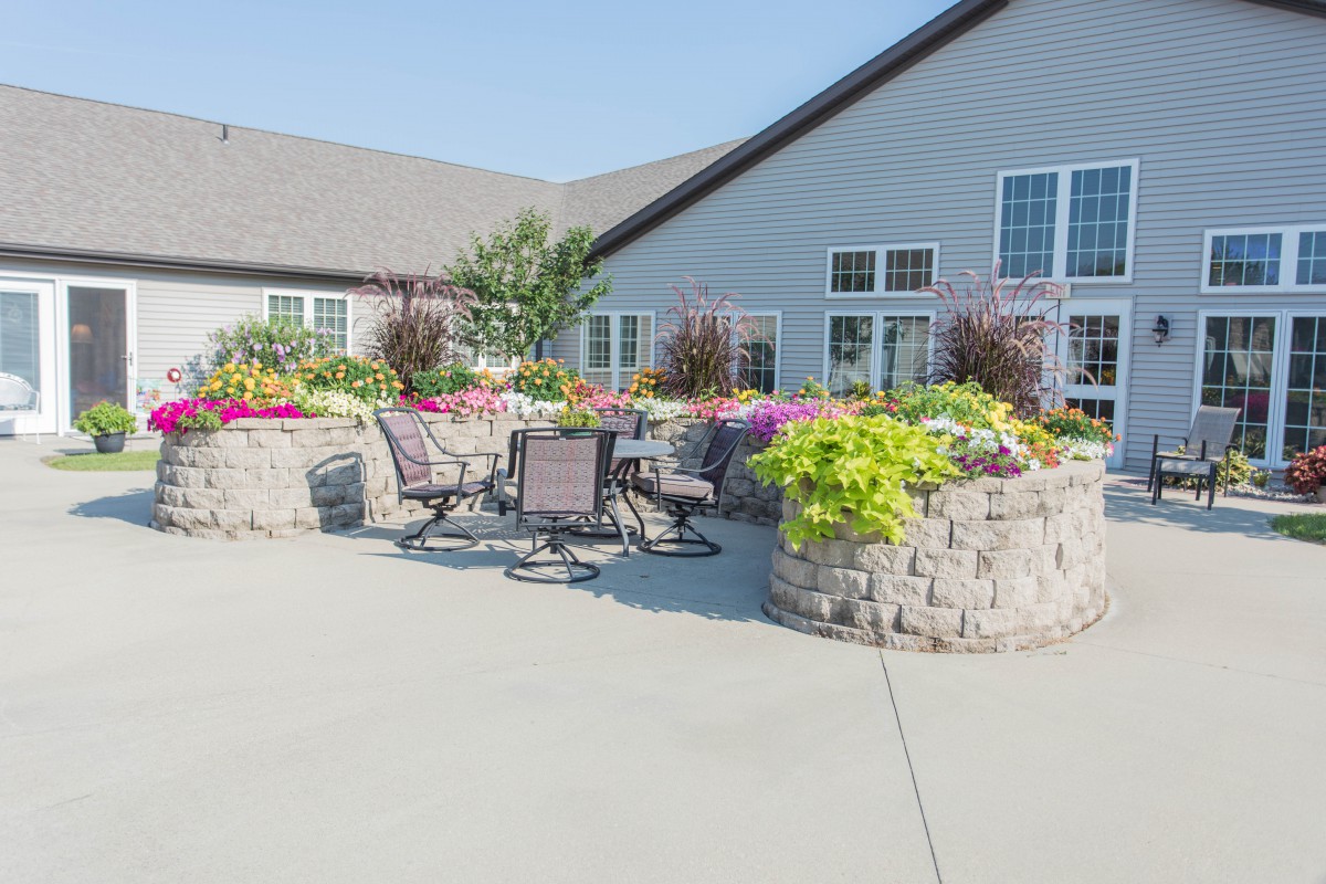 A sunny outdoor patio area with tables, chairs, and vibrant flower arrangements next to a building.