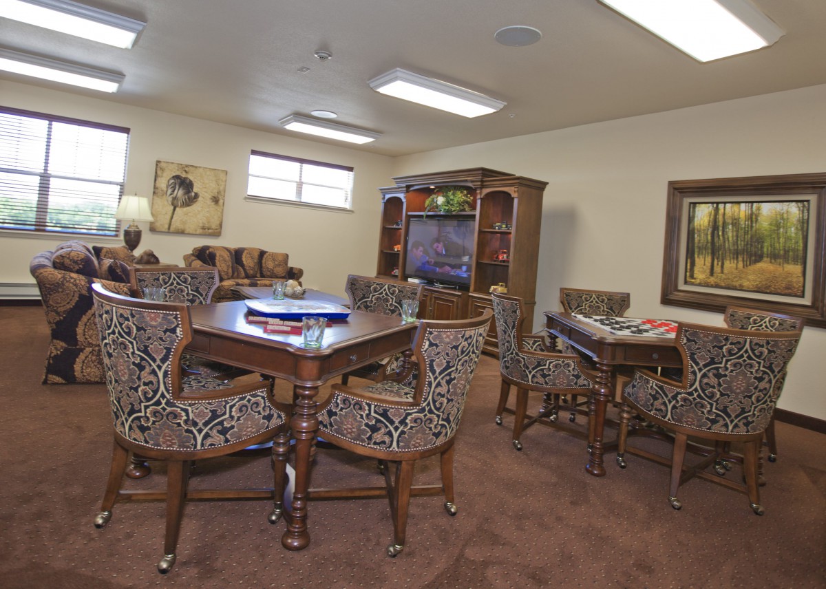 A cozy living room with patterned chairs around tables, a television stand, and framed artwork on the walls.