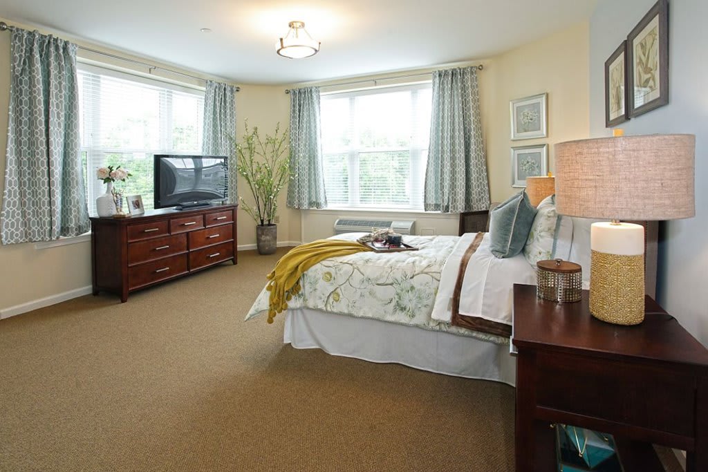 Spacious bedroom with a neatly arranged bed, television, and large windows.