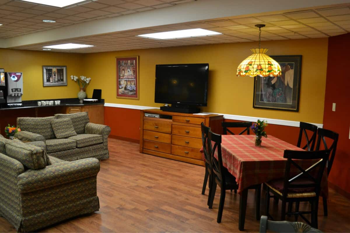A cozy basement living area featuring a television, sofa, dining table, and warm interior design with wood flooring.