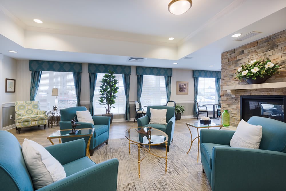 A modern living room with teal chairs and glass coffee tables, accented by large windows and green curtains.