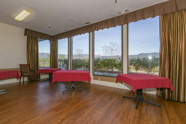 A spacious event room with large windows and red tablecloths offering views of the outdoors.