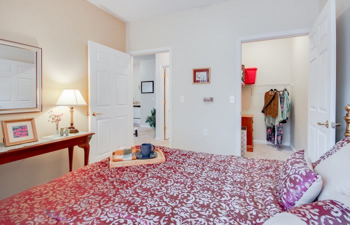 A cozy bedroom featuring a neatly made bed with a patterned blanket, a bedside table with a lamp, and an open door leading to a closet.