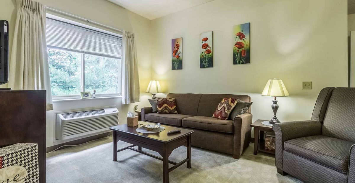 A cozy living room featuring a sofa with decorative pillows, a coffee table, two lamps, and floral artwork on the wall.