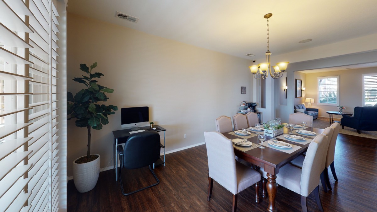 A dining room with a table set for a meal, featuring a home office corner with a computer desk.
