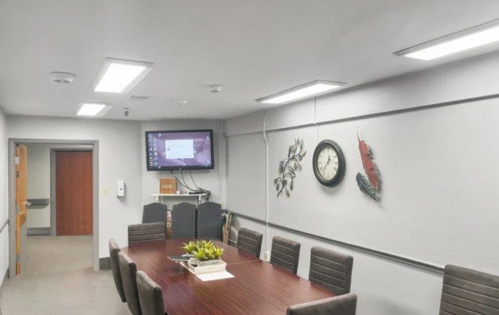 A modern conference room with a long meeting table, chairs, a wall-mounted television, and clock.