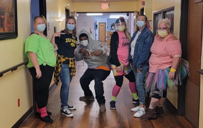 A group of people wearing masks and casual clothing pose together in a hallway.