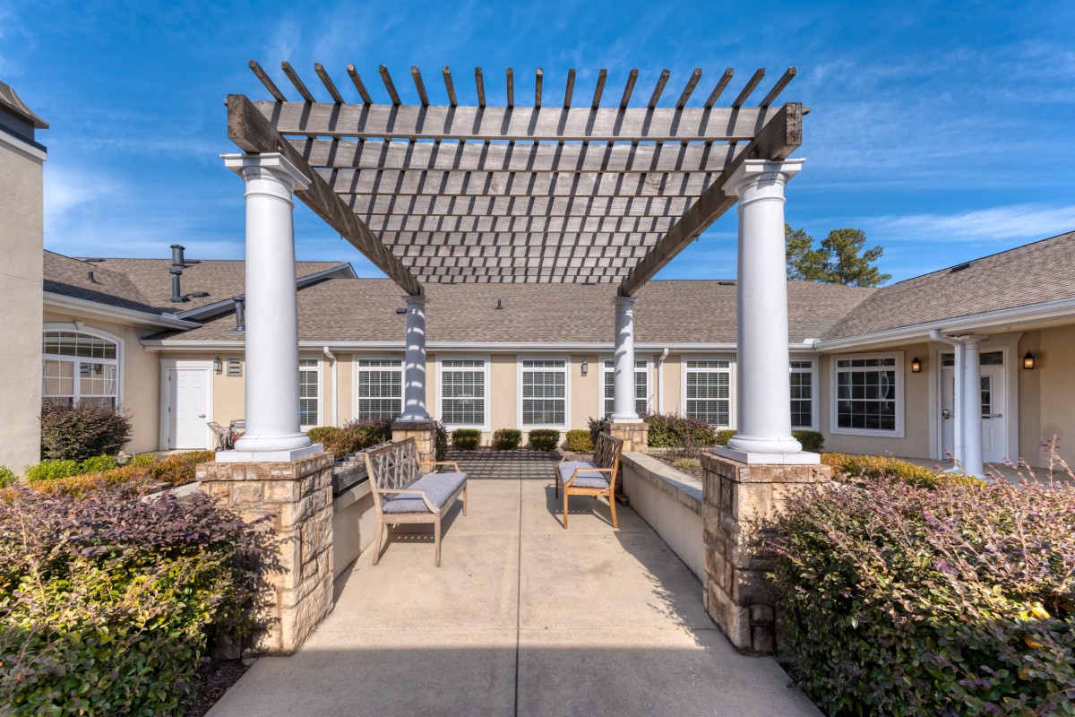 A serene outdoor patio featuring a pergola with white columns, complemented by seating and a clear blue sky.