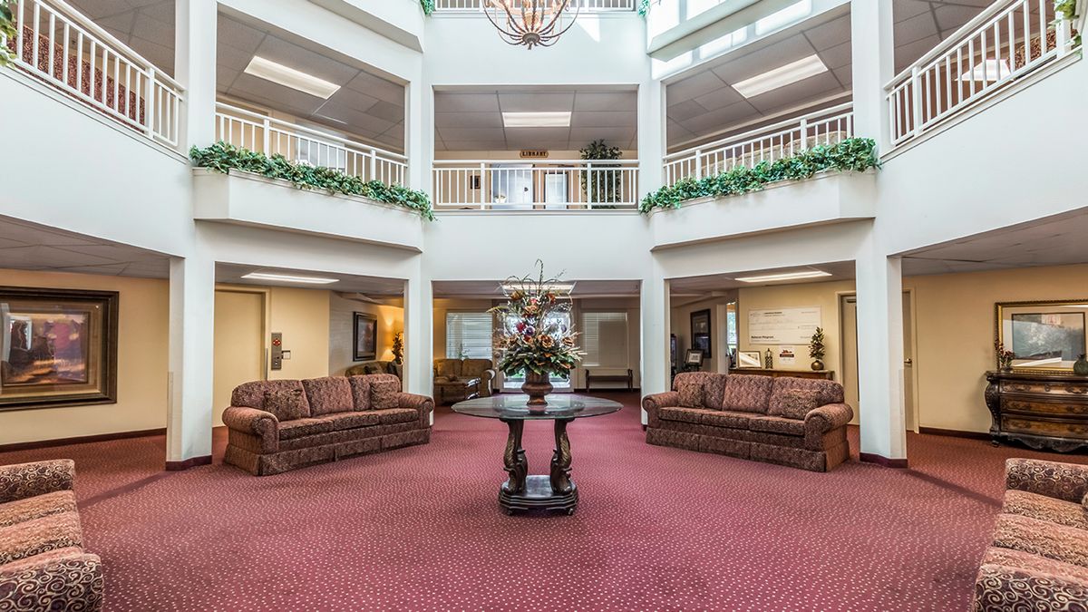 A spacious lobby area with sofas and a decorative table in the center, surrounded by balconies and greenery.